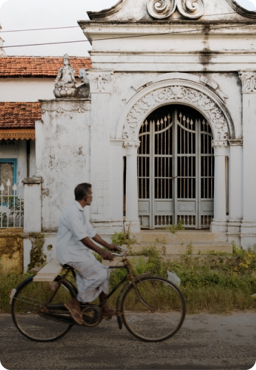 Man riding a bicycle past a historic colonial building in Sri Lanka